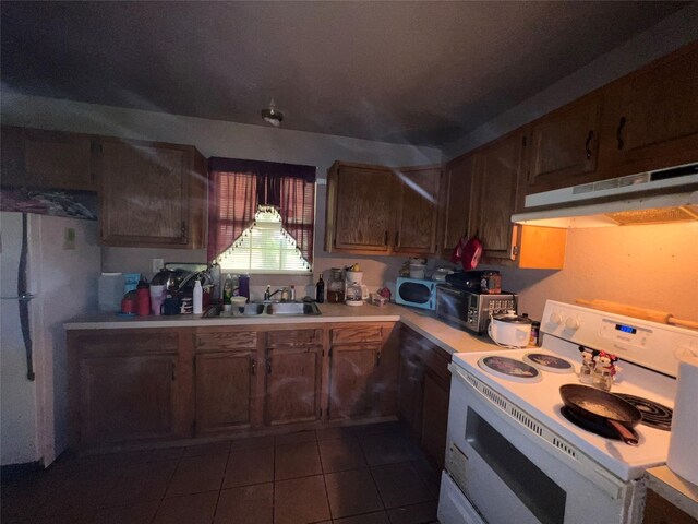 kitchen featuring light countertops, white appliances, dark tile patterned floors, under cabinet range hood, and a sink