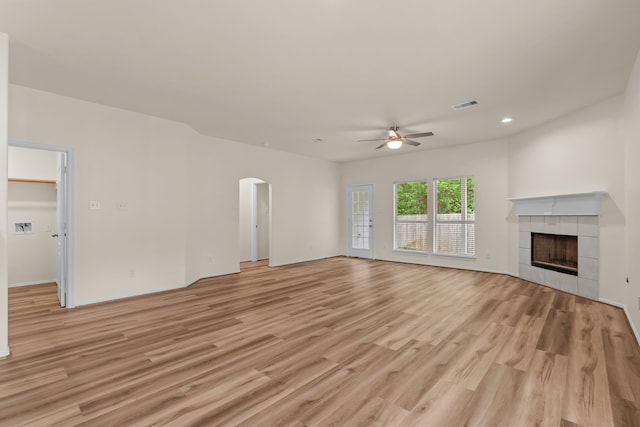 1069 Shadow Glenn Dr, Conroe, TX 77301 - unfurnished living room featuring a ceiling fan, visible vents, arched walkways, a tile fireplace, and light wood-type flooring
