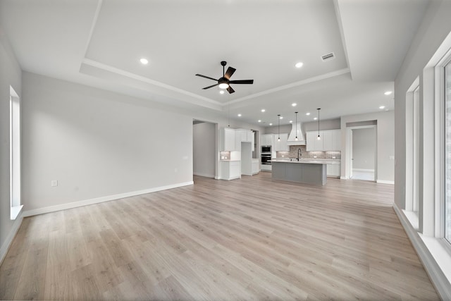 10017 Larkin Cv, Willis, TX 77318 - unfurnished living room with a raised ceiling, recessed lighting, a ceiling fan, light wood-style floors, and ornamental molding