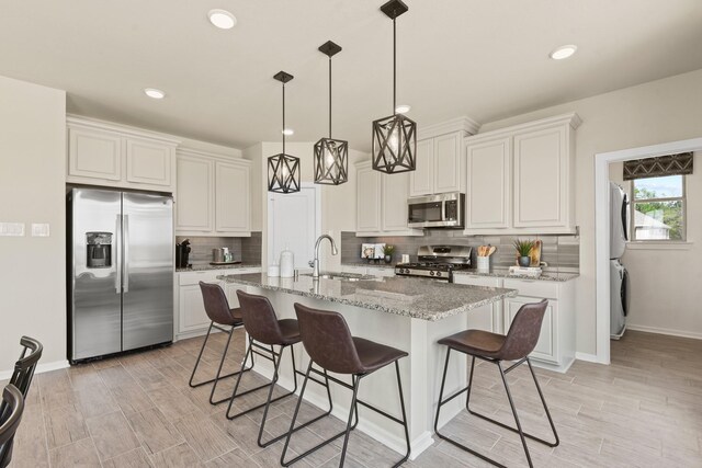 15854 Invergelder Dr, Atascocita, TX 77346 - kitchen featuring stainless steel appliances, stacked washing machine and dryer, a sink, backsplash, and a kitchen bar