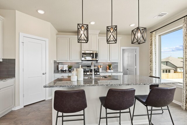 15854 Invergelder Dr, Atascocita, TX 77346 - kitchen with stainless steel microwave, a sink, tasteful backsplash, a kitchen breakfast bar, and white cabinetry