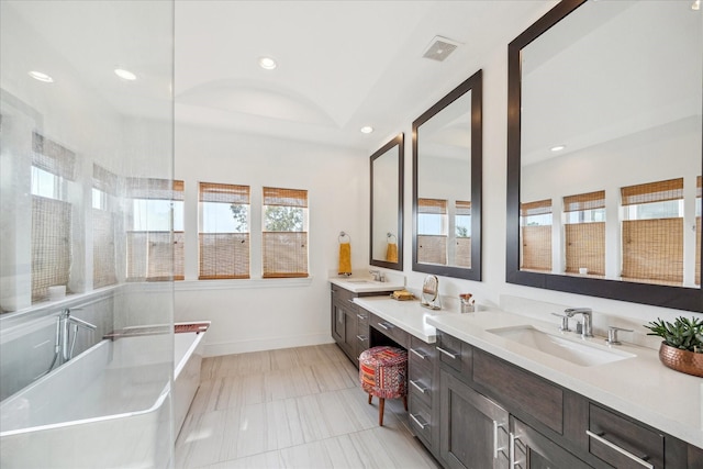 full bath featuring double vanity, recessed lighting, a sink, and a soaking tub