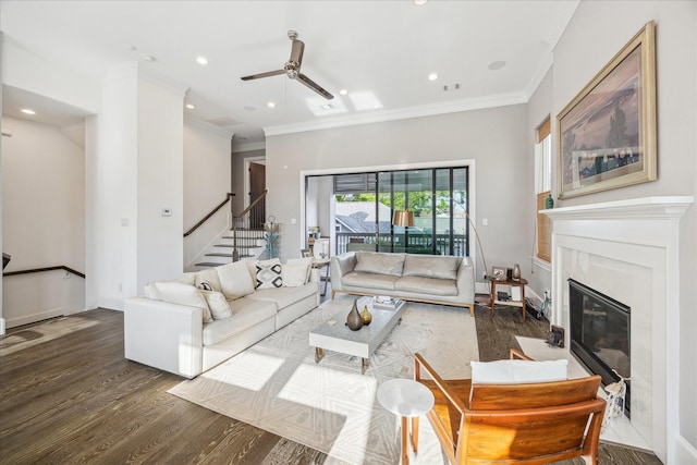living area with a ceiling fan, crown molding, a fireplace, wood finished floors, and stairs