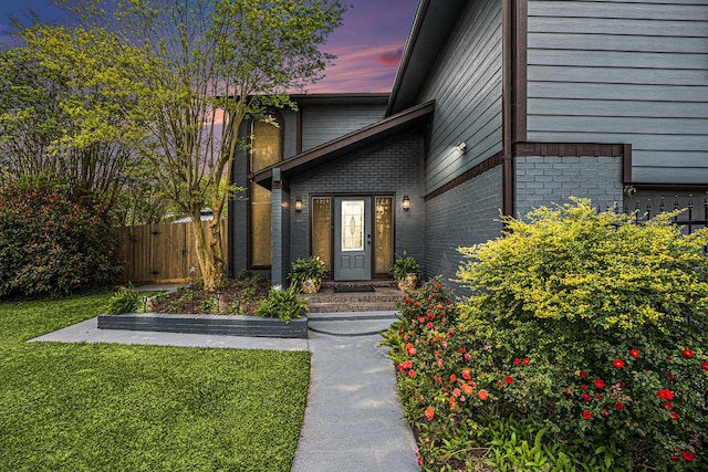 property entrance with fence, a gate, a lawn, and brick siding