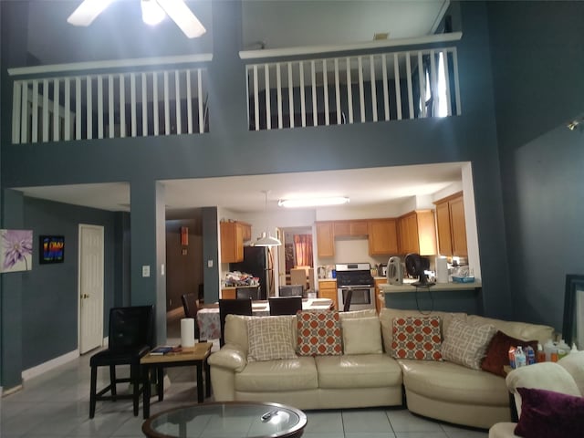 living room with light tile patterned flooring, baseboards, ceiling fan, and a high ceiling