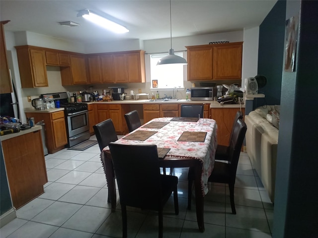 kitchen with light countertops, a sink, appliances with stainless steel finishes, brown cabinets, and light tile patterned floors