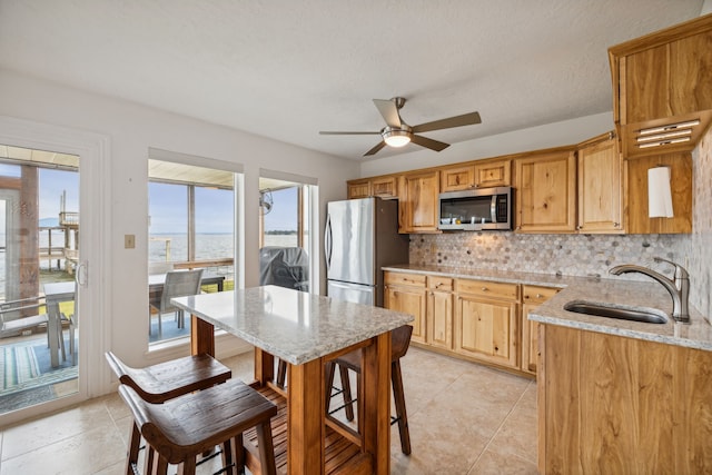 kitchen featuring ceiling fan, appliances with stainless steel finishes, tasteful backsplash, light stone countertops, and a sink