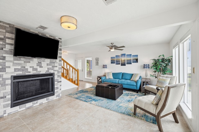 tiled living area with a stone fireplace, stairs, ceiling fan, and visible vents