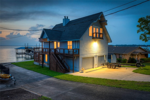 exterior space with an attached garage, a shingled roof, a water view, a chimney, and a yard