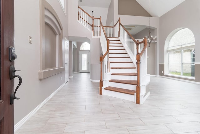 entryway with stairs, a wealth of natural light, high vaulted ceiling, and an inviting chandelier