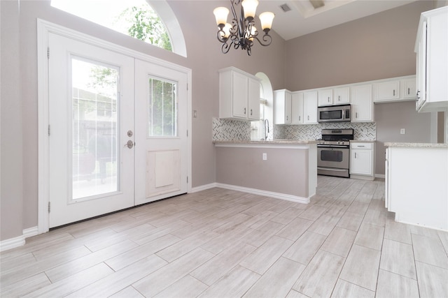 kitchen featuring backsplash, a high ceiling, stainless steel appliances, white cabinets, and an inviting chandelier