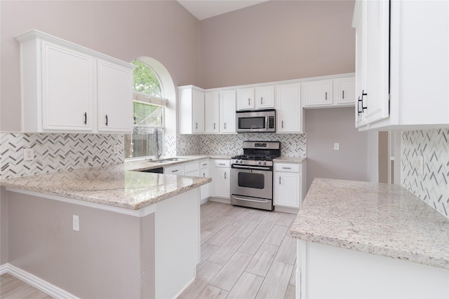 kitchen featuring white cabinetry, decorative backsplash, a sink, a peninsula, and appliances with stainless steel finishes