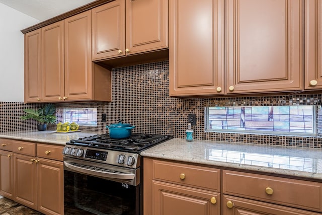 kitchen with backsplash, stainless steel gas range, and light stone counters