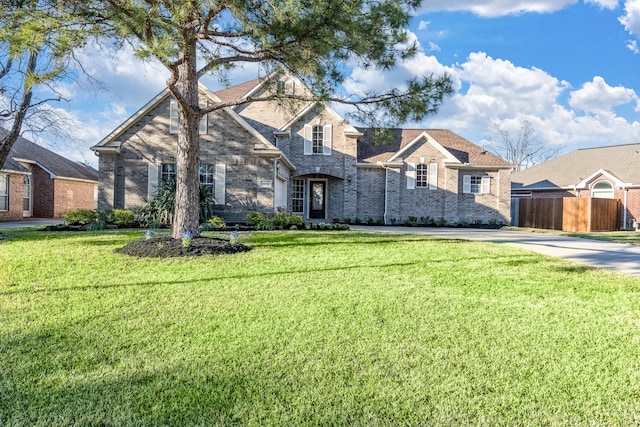 traditional-style house with brick siding, fence, a front lawn, and concrete driveway