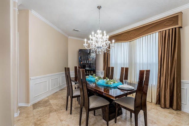 dining space with an inviting chandelier, ornamental molding, visible vents, a decorative wall, and wainscoting