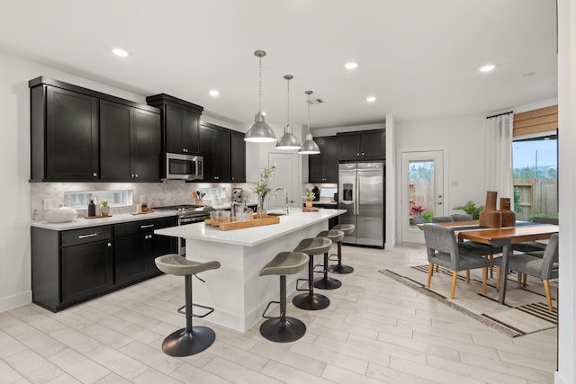 kitchen featuring dark cabinetry, a breakfast bar, appliances with stainless steel finishes, and decorative backsplash