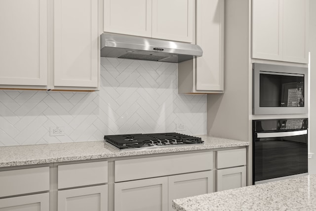 kitchen with backsplash, under cabinet range hood, black appliances, and light stone countertops