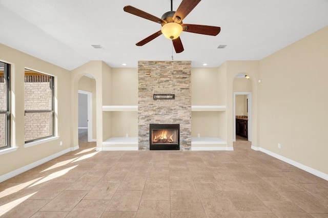 unfurnished living room with baseboards, arched walkways, visible vents, a ceiling fan, and built in features