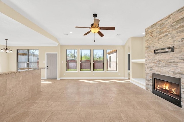 unfurnished living room with ceiling fan with notable chandelier, baseboards, and a fireplace