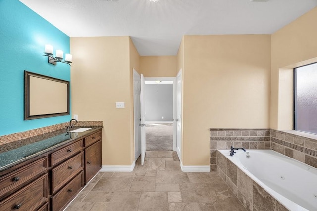 bathroom with baseboards, stone tile flooring, vanity, and a jetted tub