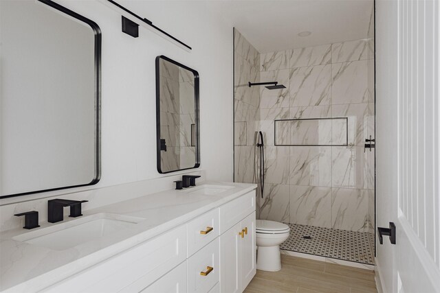bathroom featuring double vanity, a sink, a tile shower, and toilet