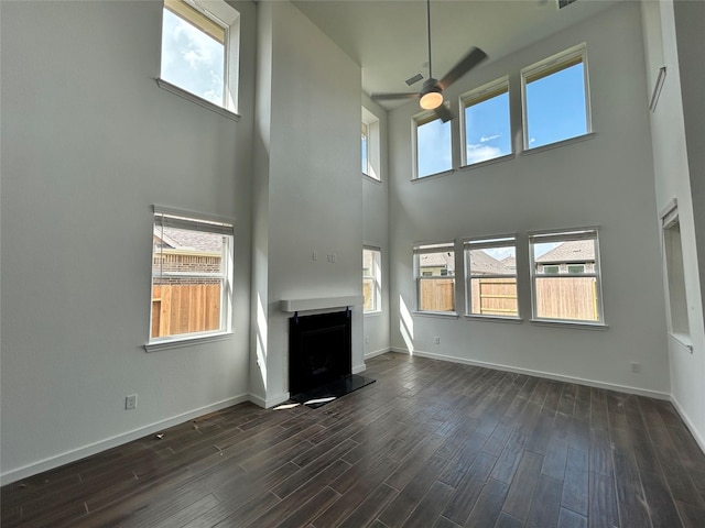 6215 Amberwood Dr, League City, TX 77573 - unfurnished living room featuring a ceiling fan, a fireplace with raised hearth, a towering ceiling, dark wood finished floors, and healthy amount of natural light