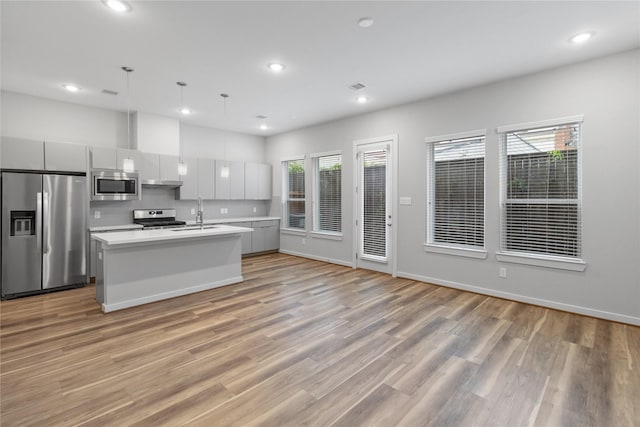 kitchen with a sink, light wood-type flooring, stainless steel appliances, a center island with sink, and light countertops