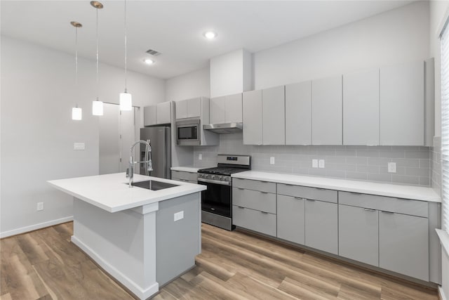 kitchen featuring an island with sink, gray cabinets, a sink, tasteful backsplash, and appliances with stainless steel finishes