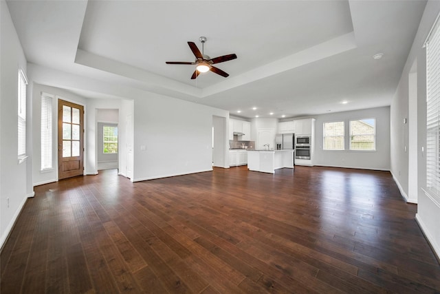29026 Zacate Creek Ln, Fulshear, TX 77441 - unfurnished living room featuring a raised ceiling, baseboards, a ceiling fan, dark wood-style flooring, and recessed lighting