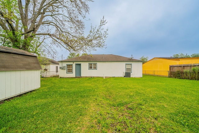back of property with central air condition unit, a lawn, an outbuilding, and fence