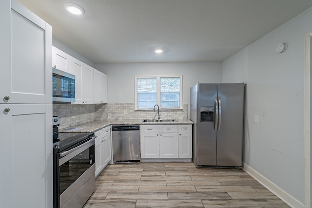 kitchen with white cabinetry, stainless steel appliances, backsplash, a sink, and light stone countertops