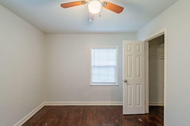 unfurnished bedroom with a spacious closet, baseboards, ceiling fan, and wood finished floors