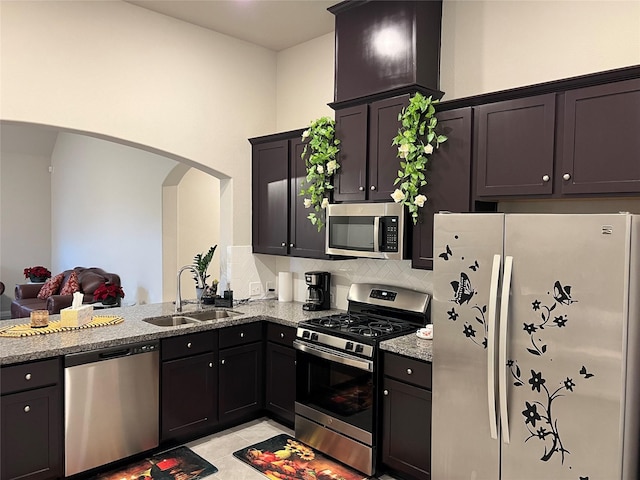 2923 Painted Sunrise Trl, Houston, TX 77045 - kitchen featuring stainless steel appliances, backsplash, a sink, arched walkways, and light stone countertops