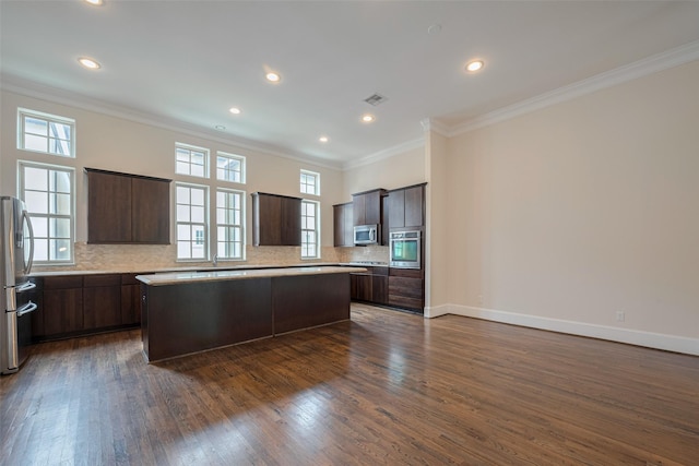 kitchen featuring crown molding, dark brown cabinets, a center island, stainless steel appliances, and decorative backsplash