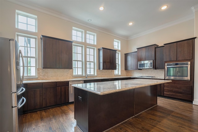 kitchen with dark brown cabinetry, appliances with stainless steel finishes, dark wood finished floors, a center island, and ornamental molding