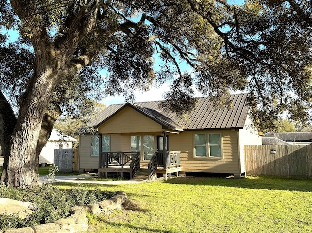 rear view of property featuring a standing seam roof, a wooden deck, fence, metal roof, and a yard