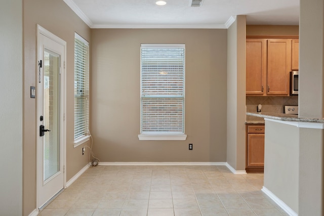 kitchen featuring light stone counters, stainless steel microwave, decorative backsplash, light tile patterned floors, and ornamental molding