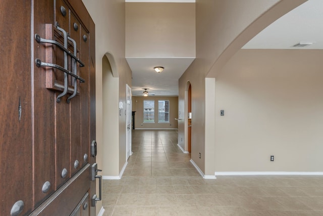 entryway featuring visible vents, light tile patterned flooring, baseboards, arched walkways, and a ceiling fan