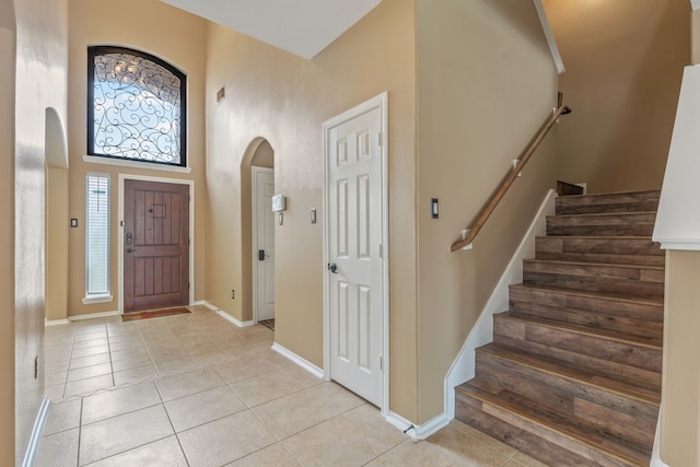 foyer entrance featuring light tile patterned floors, arched walkways, plenty of natural light, and a towering ceiling