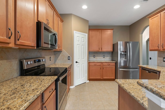 kitchen featuring stainless steel appliances, brown cabinetry, light stone counters, and decorative backsplash