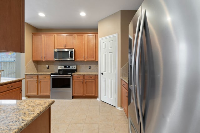 kitchen featuring appliances with stainless steel finishes, tasteful backsplash, light tile patterned flooring, and light stone counters