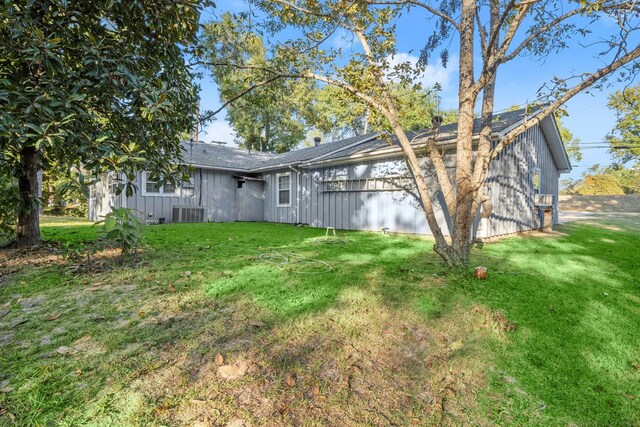 back of house featuring board and batten siding, roof with shingles, central air condition unit, and a yard