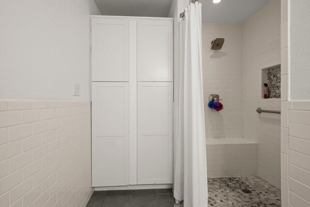 bathroom with tile patterned floors, a wainscoted wall, a stall shower, and tile walls