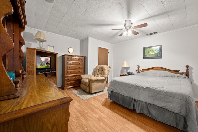bedroom with ornamental molding, visible vents, a ceiling fan, and light wood-type flooring