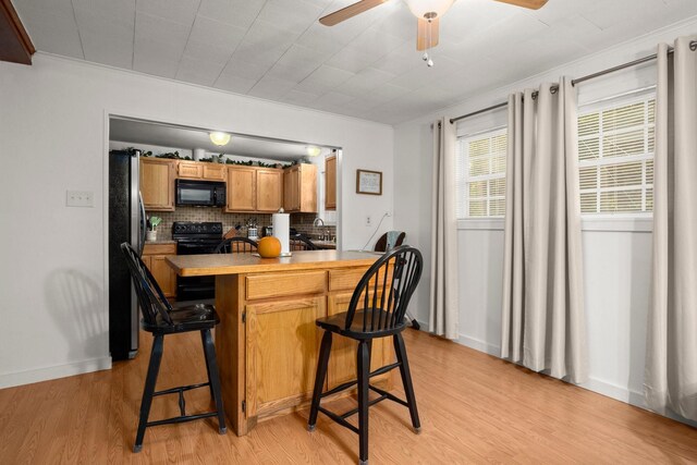 kitchen featuring backsplash, a kitchen bar, black appliances, and light wood-style flooring