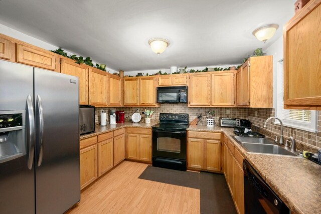 kitchen with light countertops, light wood-style flooring, tasteful backsplash, a sink, and black appliances