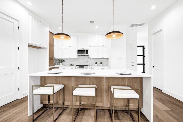 kitchen with white cabinetry, light countertops, stainless steel microwave, backsplash, and visible vents