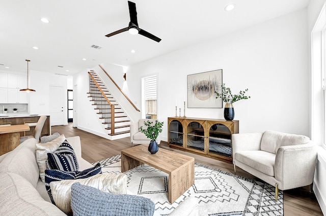 living area with stairs, visible vents, a ceiling fan, and wood finished floors