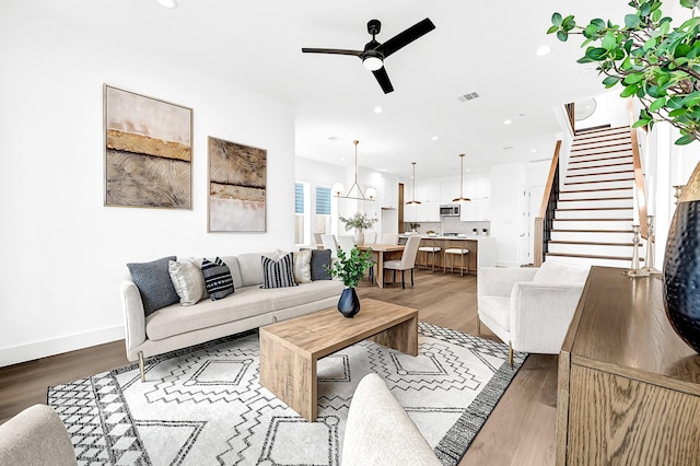 living area with stairs, visible vents, wood finished floors, and ceiling fan