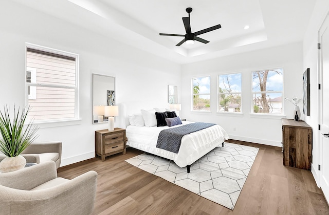 bedroom with baseboards, a tray ceiling, wood finished floors, and ceiling fan
